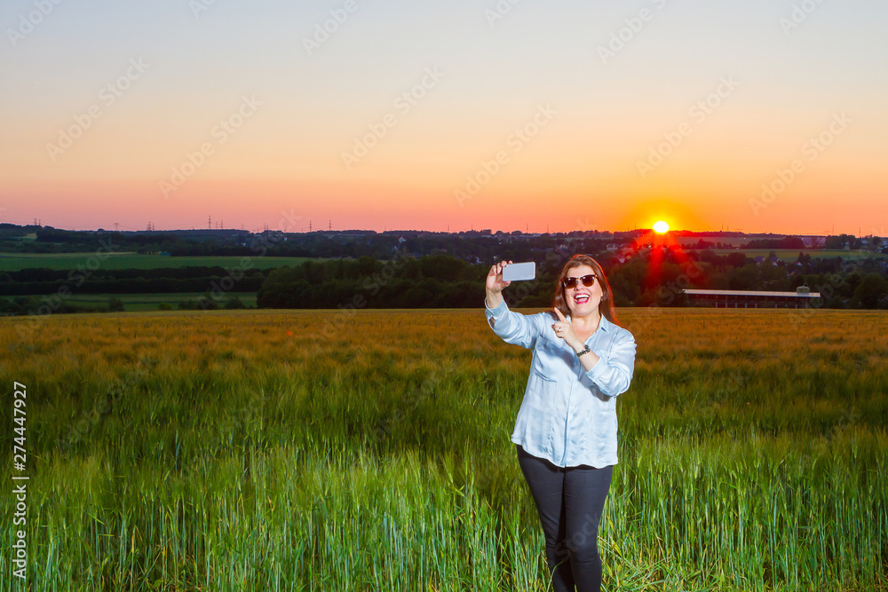 Lady is taking a selfie at the end of the day out in the field with the beautiful landscape that nature presents with the sunset.
