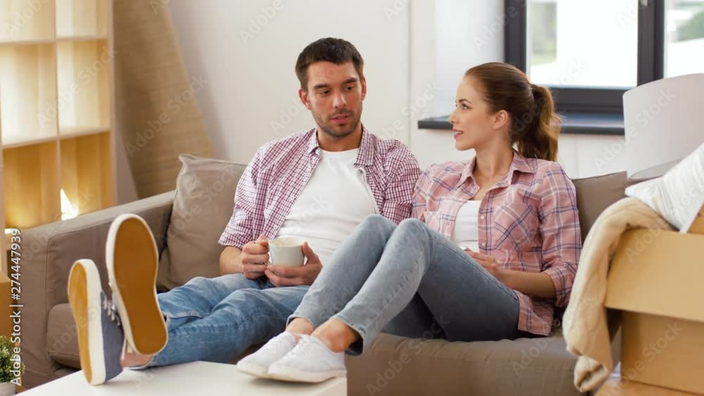 moving, people, repair and real estate concept - happy couple sitting on sofa and drinking coffee at new home moving, people, repair and real estate concept - happy couple sitting on sofa and drinking coffee at new home