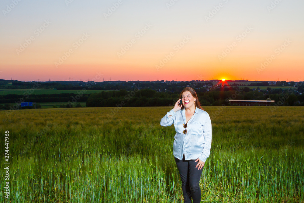 Lady is talking on the phone at the end of the day out in the field with the beautiful landscape that nature presents with the sunset.