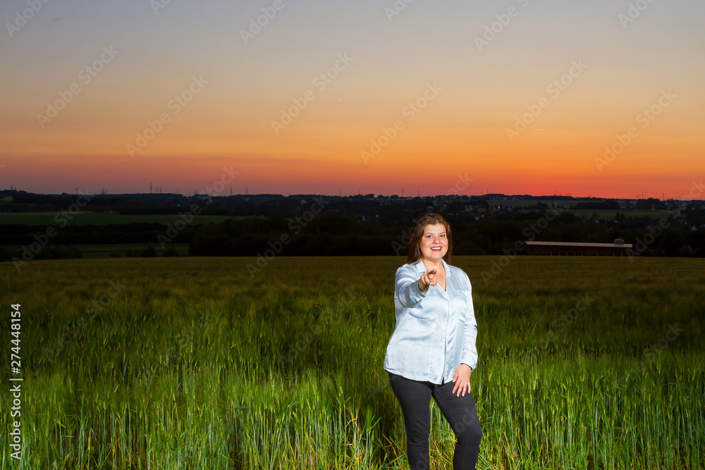 Lady points the finger at you at end of the day out in the field with the beautiful landscape that nature presents with the sunset.
