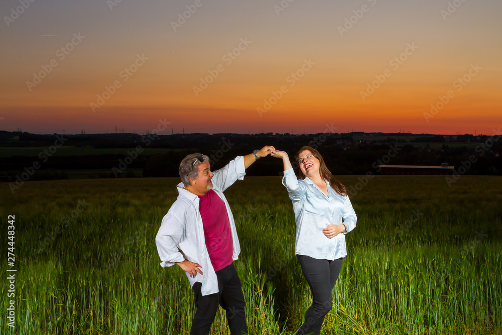 Man and woman dance together in an open field at end of the day out in the field with the beautiful landscape that nature presents with the sunset.