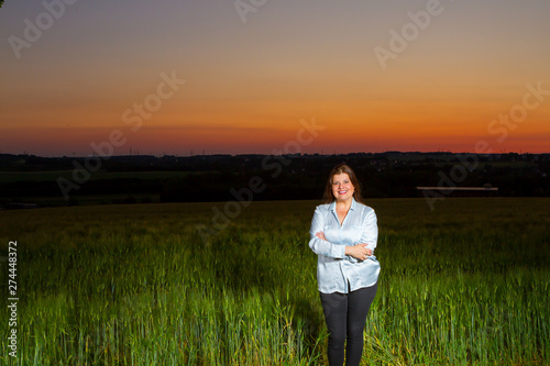 Beautiful lady poses standing at end of the day out in the field with the beautiful landscape that nature presents with the sunset. © Alejandro