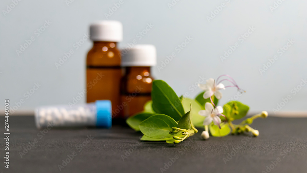 Alternative medicines - Homeopathic sugar globules and liquid substance bottles with green leaves and white flower Alternative medicines - Homeopathic sugar globules and liquid substance bottles with green leaves and white flower