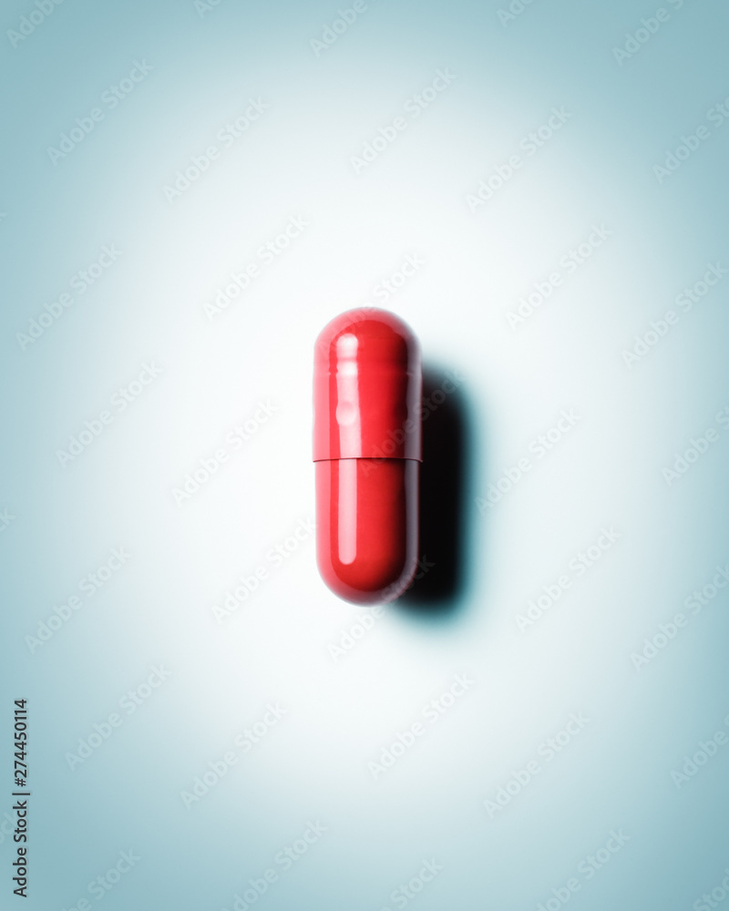 Single red capsule on blue grey background. Conceptual image for healthcare and pharmaceutical industry,