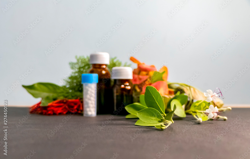 Homeopathic Concept - Blurred image of homeopathic medicine bottles with white,red,orange flowers and green leaves