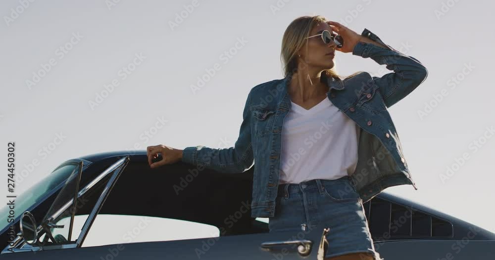 Attractive model woman in denim jacket flipping her hair and leaning on classic vintage sports car
