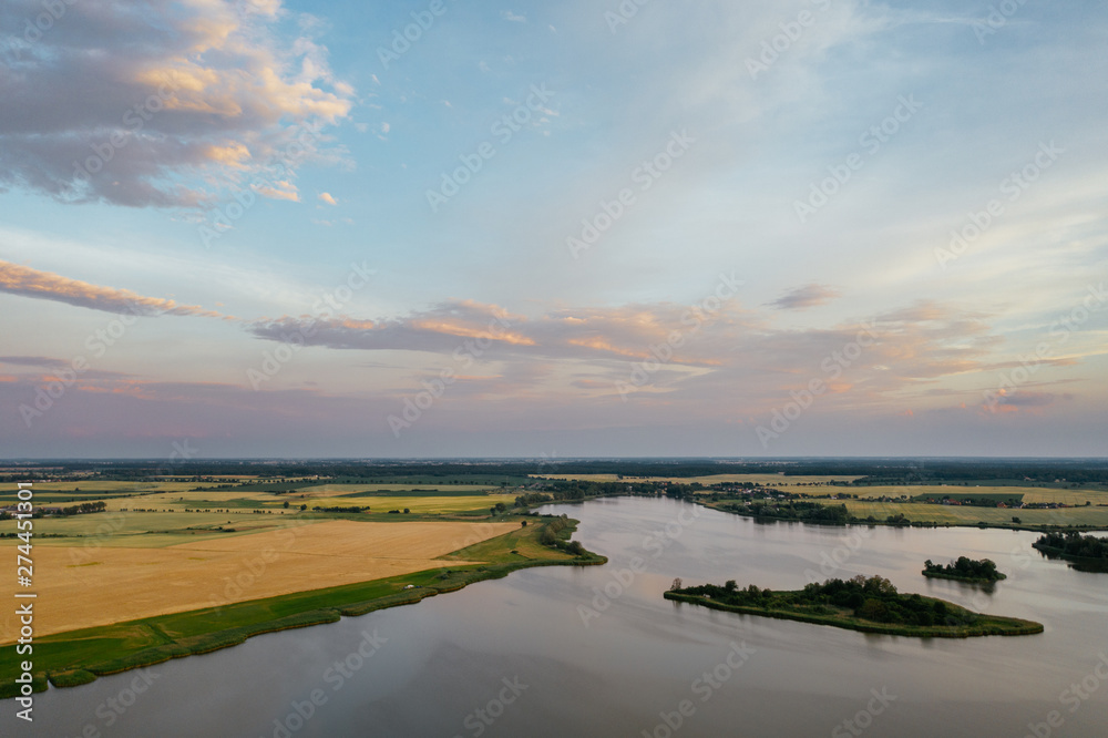 Fototapeta premium Sunset over the lake in western Poland, view of agricultural fields and water.