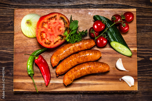 Raw sausages and vegetables on cutting board