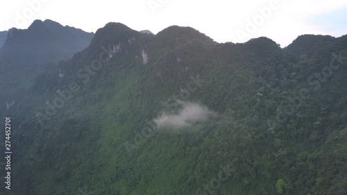 little gray cloud stuck on high peak of mountain range with tropical forest under bright sky aerial view photo