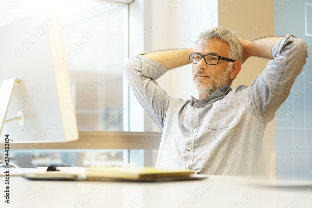 Obraz premium Relaxed businessman sitting at desk with arms behind head