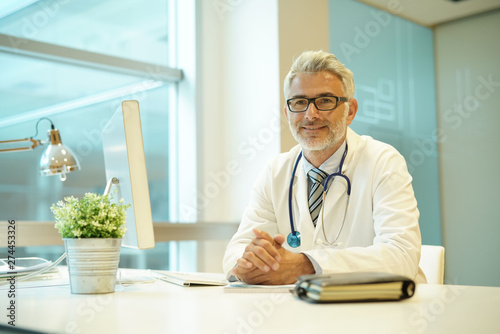 Portrait of handsome mature doctor sitting at desk in modern office photo