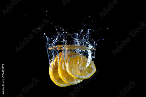 Lemon slices falling into water with splashes, isolated on black background
