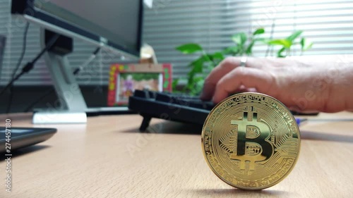 Bitcoin currency coin and a businessman using a computer keyboard consulting stock market fluctuation values.