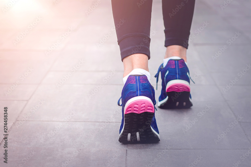 Morning running. Young lady running on a rural road during sunset in blue sneakers with black sole. Healthy lifestyle. Sports training concept Morning running. Young lady running on a rural road during sunset in blue sneakers with black sole. Healthy lifestyle. Sports training concept