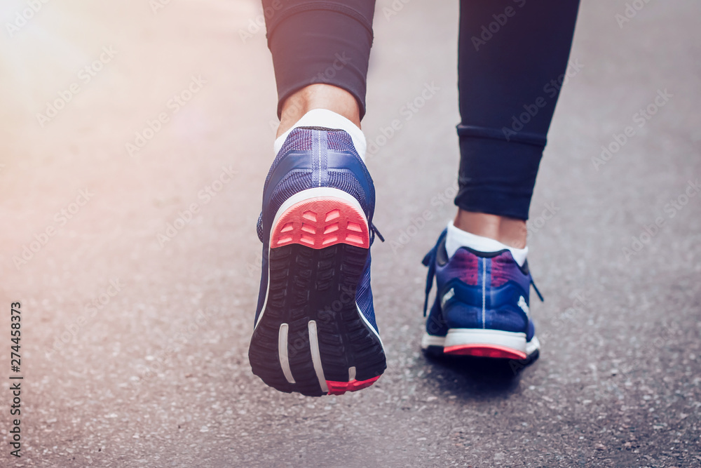 Morning running. Young lady running on a rural road during sunset in blue sneakers with black sole. Healthy lifestyle. Sports training concept