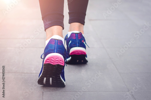 Morning running. Young lady running on a rural road during sunset in blue sneakers with black sole. Healthy lifestyle. Sports training concept