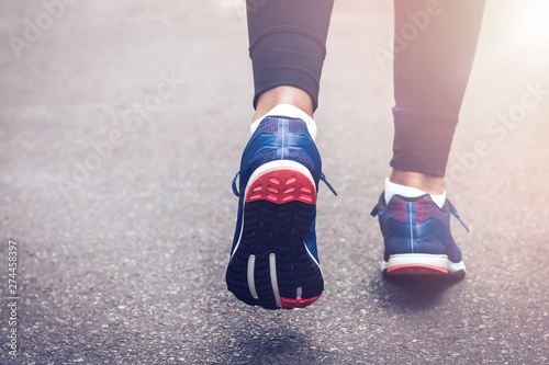 Morning running. Young lady running on a rural road during sunset in blue sneakers with black sole. Healthy lifestyle. Sports training concept