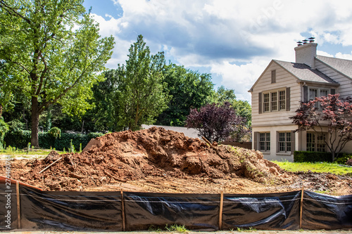 Construction  - Pile of dirt in vacant lot behind black plastic fence in upscale neighborhood with parts of adjacent houses and trees and fences visible - selective focus