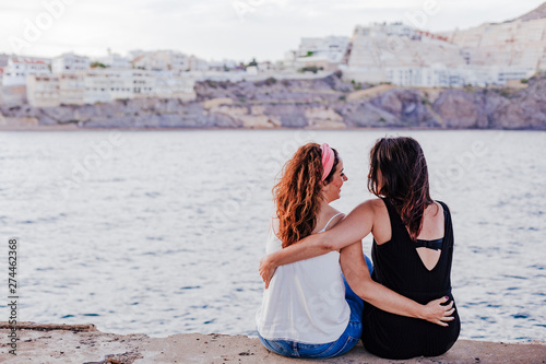 two women friends sitting by the beach hugging. lifestyle concept outdoors