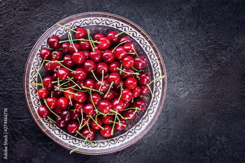 cherry berries in a plate on a dark background top view. copy space. cherry flat lay. ripe cherries background
