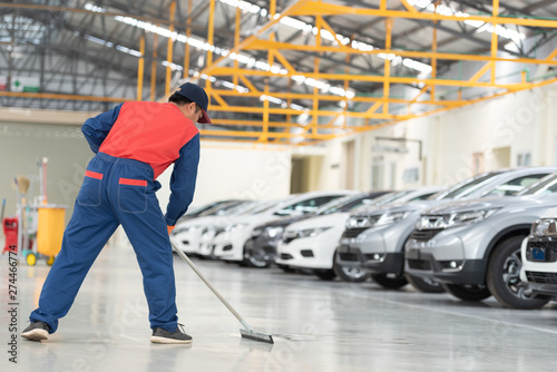The man in the repairman is holding a mop in a white suit, cleaning the protective clothing of the new epoxy floor in an empty warehouse or car service center.