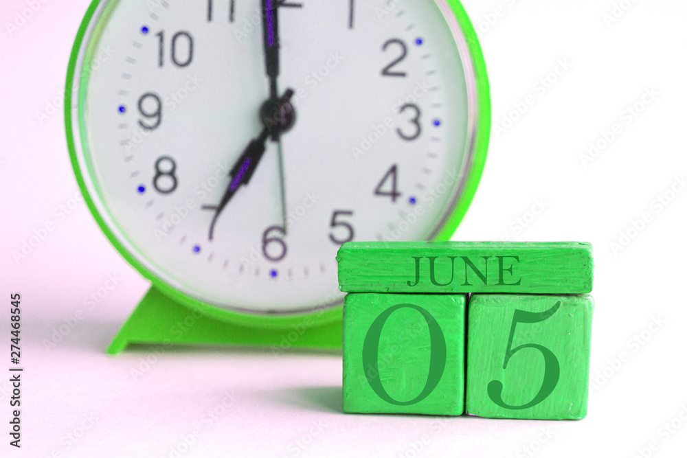 Fototapeta premium june 5th. Day 5 of month, handmade wood calendar and alarm clock on light green color. summer month, day of the year concept