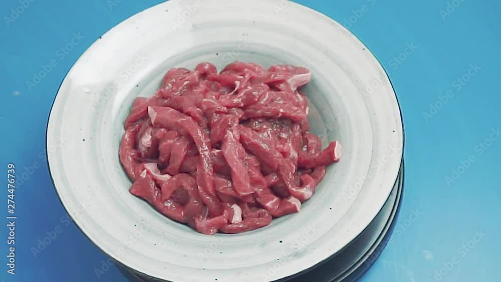 Raw meat rotating on blue background. Uncooked fresh meat cut into thin strips. Beef stroganoff in gray plate Raw meat rotating on blue background. Uncooked fresh meat cut into thin strips. Beef stroganoff in gray plate