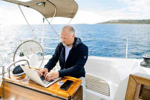 Digitaler Nomade auf einem Segelboot arbeitet konzentriert am Laptop