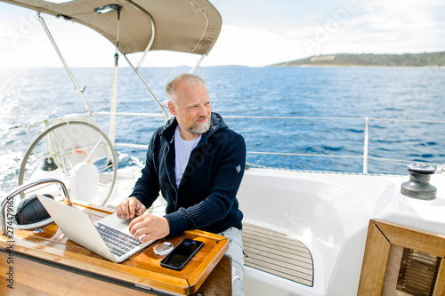 Digitaler Nomade auf einem Segelboot arbeitet konzentriert am Laptop und sieht nach vorne