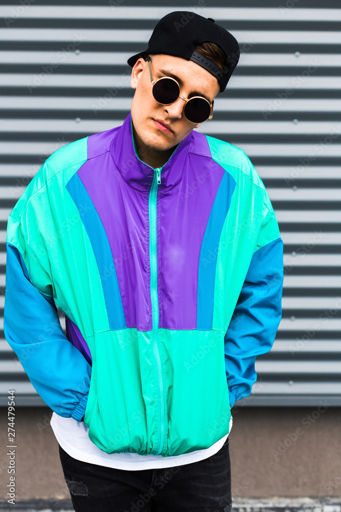 Back in time 90s 80s. Stylish young man in a retro jacket and with a  vintage cassette player, on the background of a steel wall, fashion trends,  street image Stock Photo