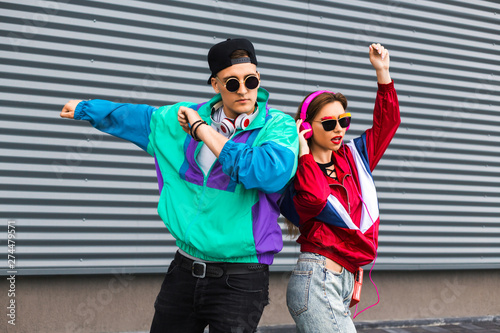 Back in time 90s 80s. Stylish young man in a retro jacket and a girl in red and with a vintage cassette player, against a steel wall, fashion trends, a street image photo