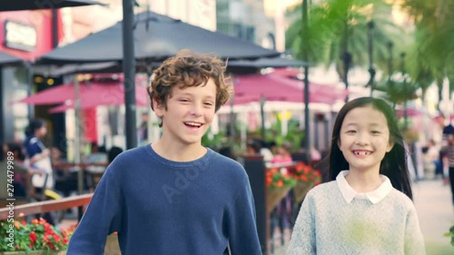 little caucasian boy and asian girl walking hand in hand on street photo