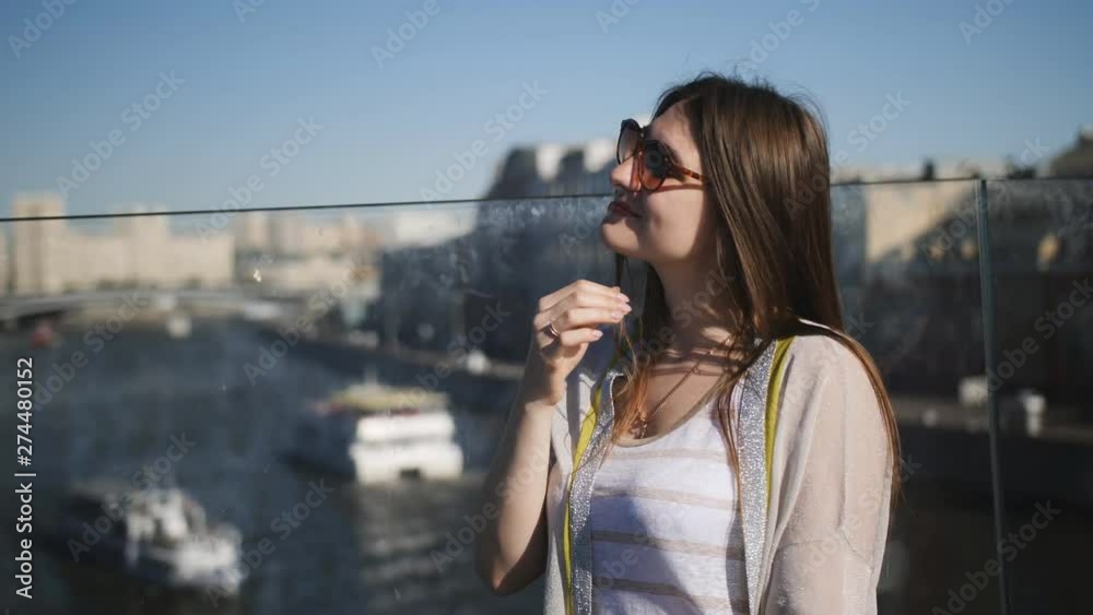 Young caucasian woman squints at city bridge over river, warm summer day Young caucasian woman squints at city bridge over river, warm summer day