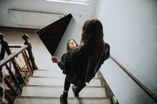portrait of brunette woman walking down the stairs while holding a mirror