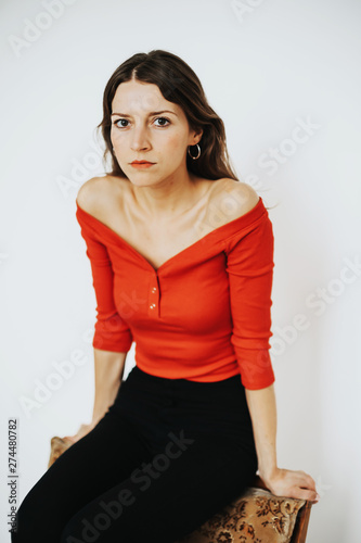 serious looking brunette woman wearing red top sitting on chair