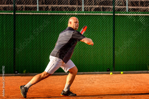 A middle-aged bald man plays tennis on the outdoor court. Sunny day. © Анна Демидова
