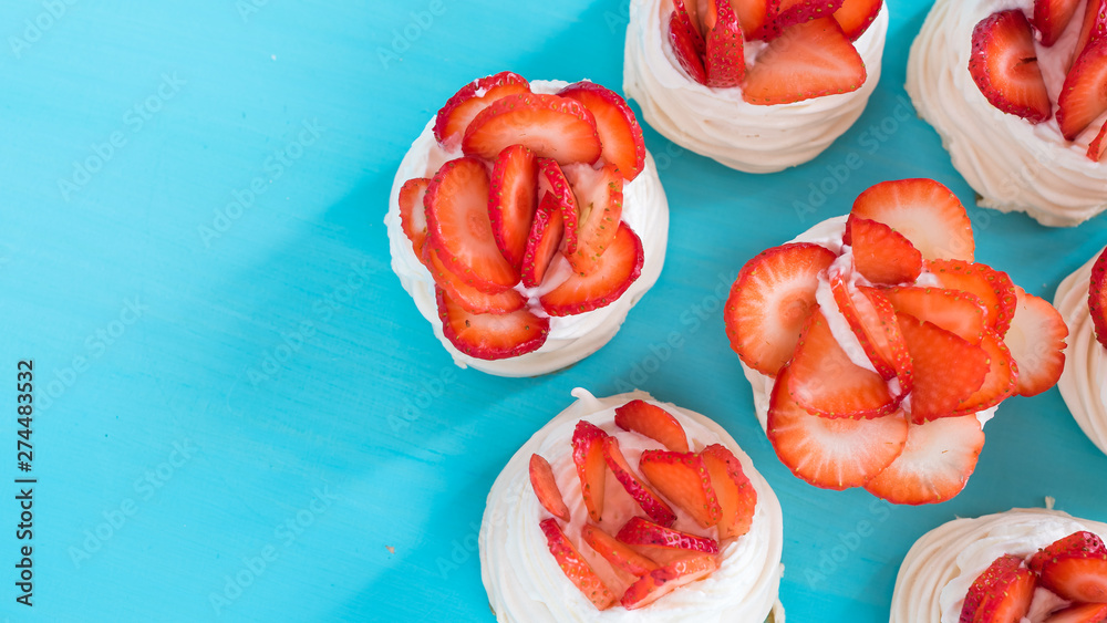 A small meringue Pavlova dessert with some strawberry slices on a blue background. Top view. A small meringue Pavlova dessert with some strawberry slices on a blue background. Top view.