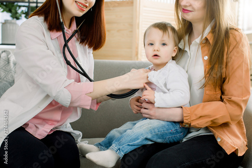 Surprised cute baby girl being checked by a female doctor using a stethoscope in clinic