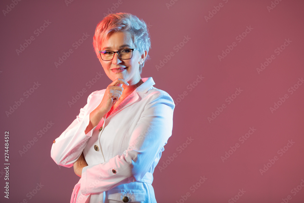 beautiful stylish woman aged, wearing glasses, in a white jacket on a pink background beautiful stylish woman aged, wearing glasses, in a white jacket on a pink background