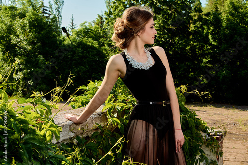 Young attractive woman in the sexy see-through, transparent, transpicuous, diaphanous, clear black dress posing at summer sunny day outdoor in the old park. Fashion woman. Young woman modern portrait. photo