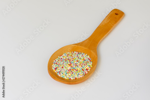 Una cuchara de madera con bolas de azücar de colores para postres