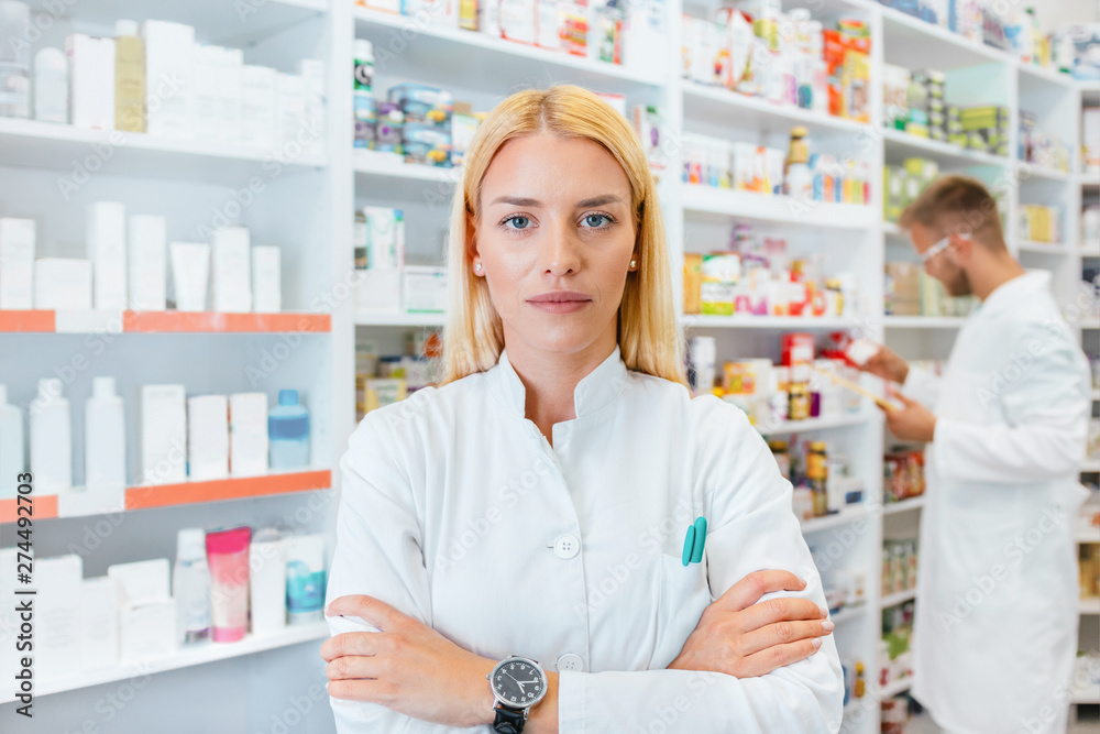 Portrait of a female pharmacist, male colleague working with drugs in the background. Portrait of a female pharmacist, male colleague working with drugs in the background.