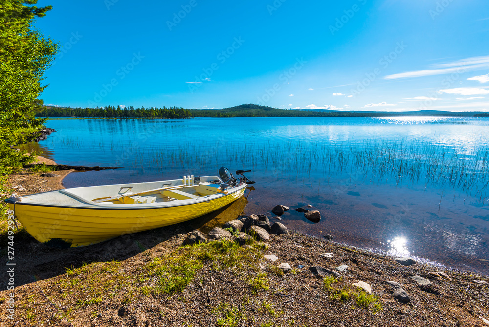 The motor boat in the border of Siebdniesjavrrie lake Swedish Lapland. The sun is reflecting in the water. Vasterbotten county, Norrland, Sweden.