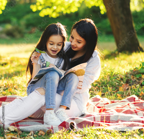 Young latin mother and daughter laughing in city park and read book