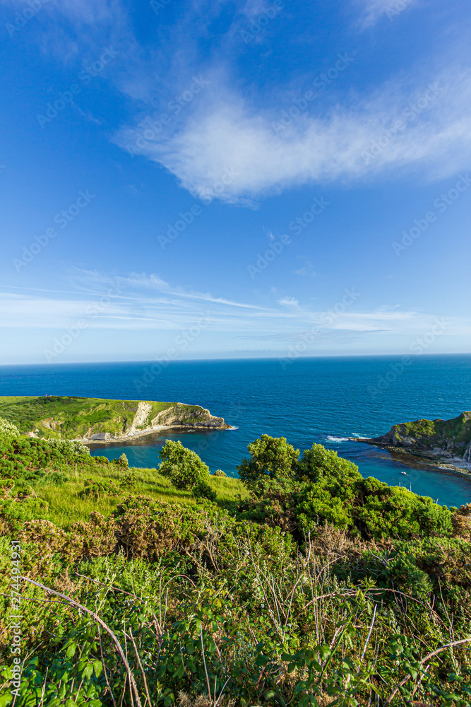 A view of the Lulworth Cove along the Jurrassic Coast in Dorset under a majestic blue sky and some white clouds.