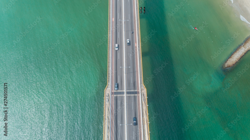 Aerial view of car driving on a bridge with natural forest trees, sand, tropical beach and waves rolling into the shore.