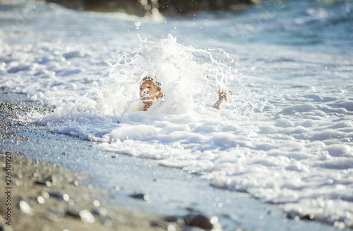 Young girl playing in breaking waves on beach. Big wave covering girl playing on sand.