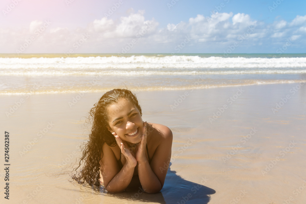 Happy healthy beautiful Brazilian multiracial woman lying down on sand enjoying sun tanning sunbathing in swimsuit relaxing on Brazil tropical beach summer vacation. Smiling laughing girl. Happy healthy beautiful Brazilian multiracial woman lying down on sand enjoying sun tanning sunbathing in swimsuit relaxing on Brazil tropical beach summer vacation. Smiling laughing girl.