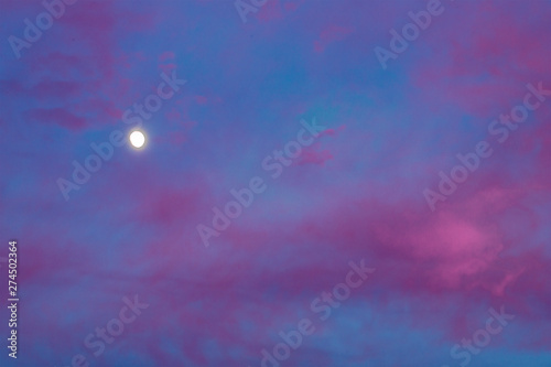 Moonrise in a pink cloudy sky after sunset. View of the summer sky at sunset at the end of the day.