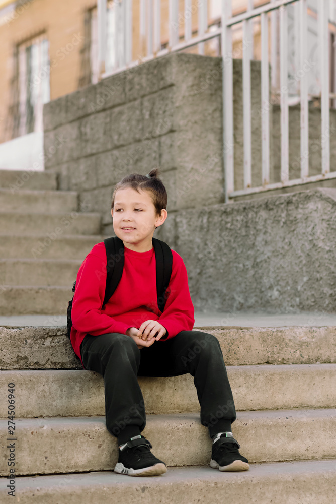 A smiling boy with a backpack on his back is sitting on the steps of the stairs. Back to school. Happy student. A smiling boy with a backpack on his back is sitting on the steps of the stairs. Back to school. Happy student.